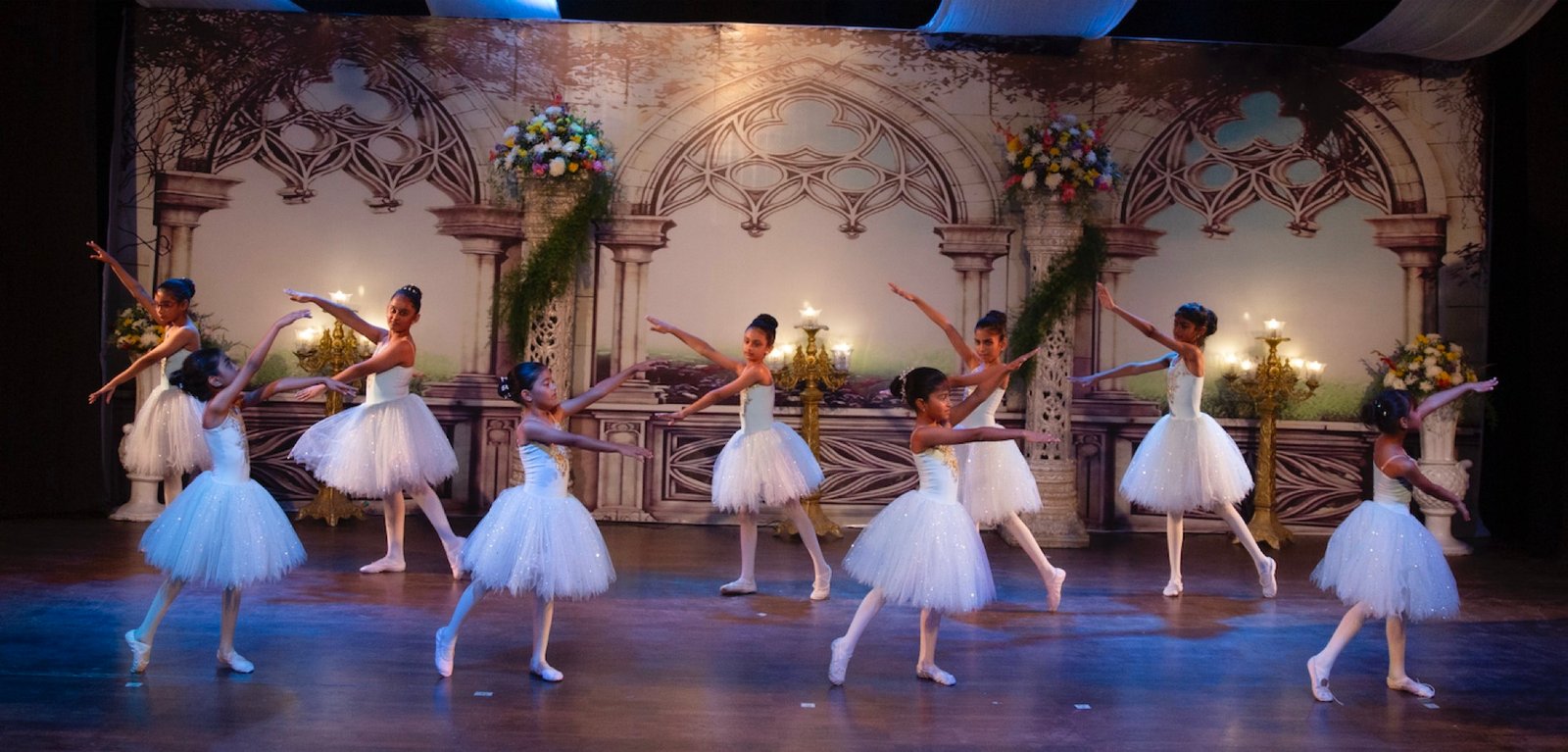Young ballerinas performing on stage during annual recital under spotlight